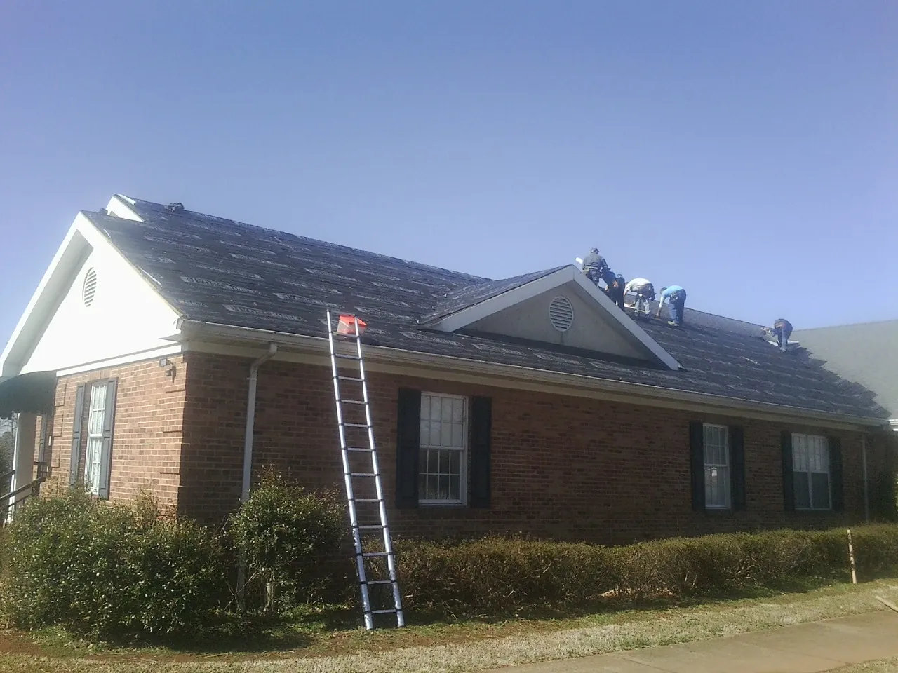 Crew tearing shingles off a brick ranch roof with a ladder set — Emergency Roof Repair work by our crew in Englewood