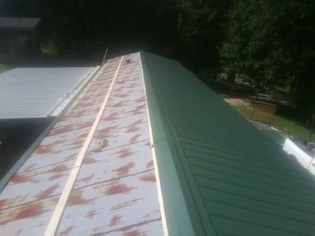 Old rusted panels beside newly installed green metal roofing — Wind Damage Roof Repair by Roofing Brothers in Englewood